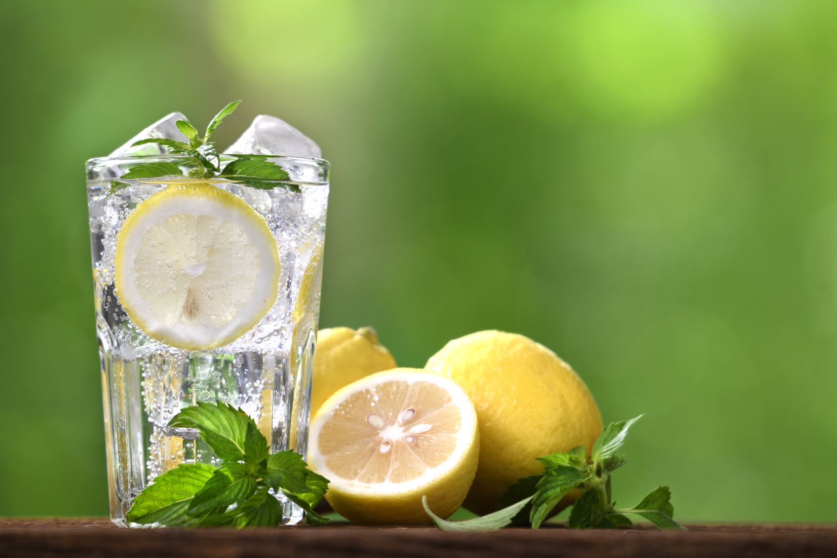 Lemon soda with sliced lemon in glass on nature background